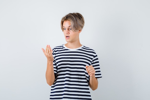 Free photo portrait of pretty teen boy looking at his palm in striped t-shirt and looking shocked front view