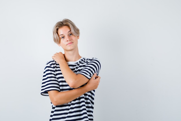 Free photo portrait of pretty teen boy stretching arms in striped t-shirt and looking thoughtful front view