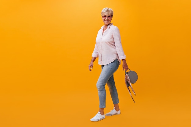 Free Photo portrait of pretty woman in jeans and shirt posing with bag on orange background