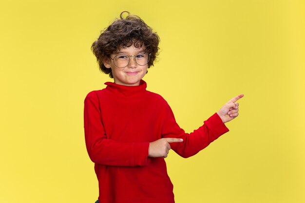 Portrait of pretty young curly boy in red wear on yellow studio wall