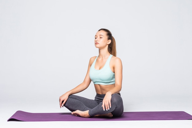 Portrait of pretty young woman doing yoga exercise meditation on mat isolated