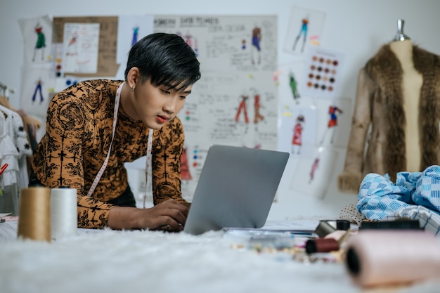 Portrait of Professional Asian young male tailor with measuring tape on neck working on laptop