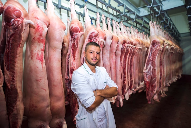 Portrait of professional butcher in factory cold storage holding arms crossed with pig carcass behind