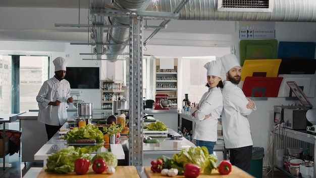 Portrait of professional chefs posing with arms crossed on camera, working in restaurant kitchen to make dish meal. Man and woman in uniform being professional cooks, preparing culinary recipe.