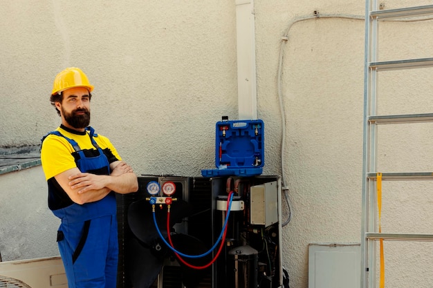 Free photo portrait of professional engineer standing in front of fixed air conditioner, proud of work done. skilled technician contracted by customer happy with smooth maintenance of hvac system components