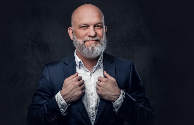 Portrait of professional old man dressed in suit pulling his jacket against dark background.