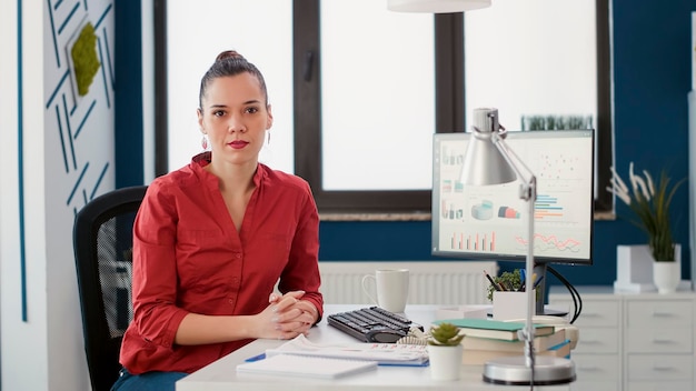 Portrait of project manager sitting at office desk to work on business growth with financial charts and sales statistics. Marketing consultant analyzing e commerce diagrams on computer.