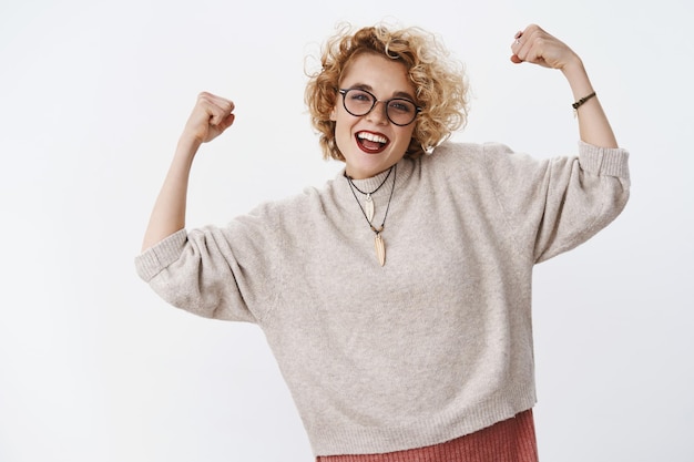 Portrait of proud girl feeling joy of winning prize raising hands mighty like champion celebrating victory and triumphing smiling broadly and cheering carefree over white wall.