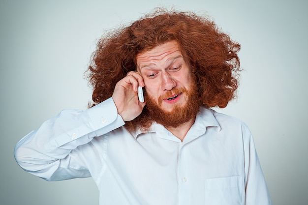 Portrait of puzzled man talking on the phone  a gray background