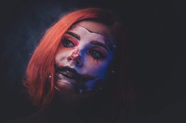 Portrait of red hair girl with spooky makeup for Halloween at dark photo studio.