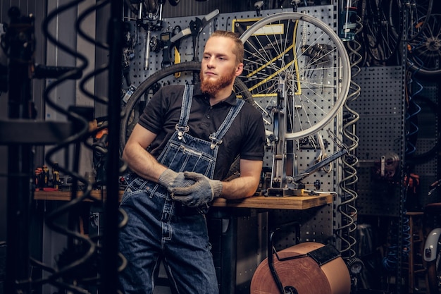 Free Photo portrait of red head bearded bicycle mechanic in a workshop with bike parts and wheel on a background.