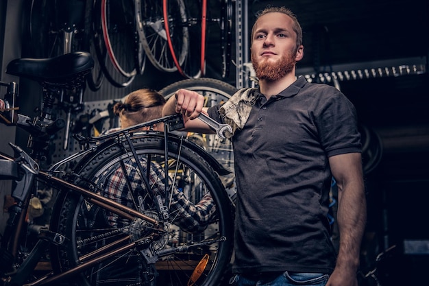 Free Photo portrait of red head bearded bicycle mechanic in a workshop with bike parts and wheel on a background.