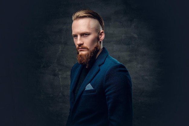 Portrait of redhead bearded hipster male dressed in a blue jacket over grey background.