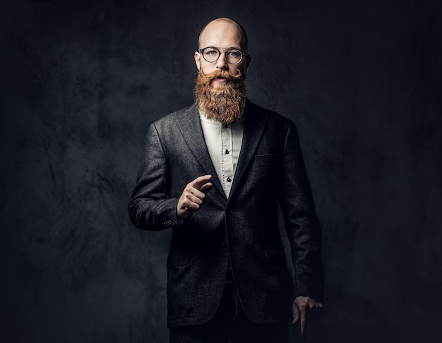 Portrait of redhead bearded male in eyeglasses dressed in an elegant wool suit over grey background.