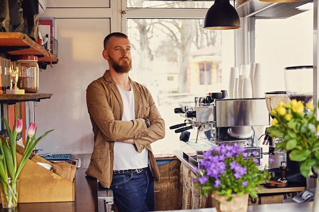 Portrait of redhead bearded male in a small cafe with a lot of flowers and coffee machine.