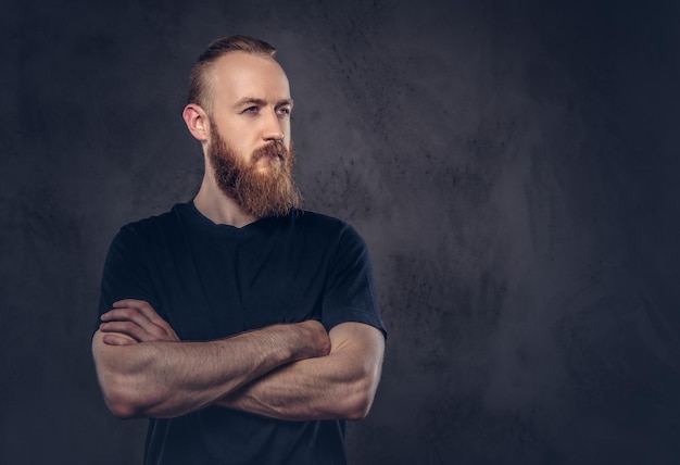 Free photo portrait of a redhead bearded man dressed in a black t-shirt standing with crossed arms. isolated on the dark textured background.