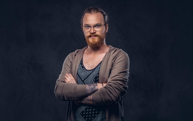 Portrait of a redhead hipster male dressed in casual clothes with glasses and full beard, standing with crossed arms in a studio. Isolated on a dark background.