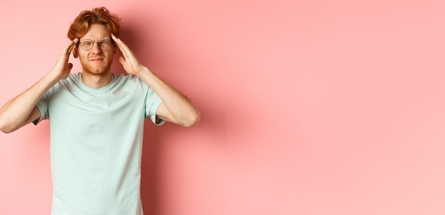 Free photo portrait of redhead man in crooked glasses touching head and feeling dizzy or nauseous having hangov