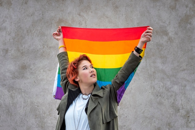 Free photo portrait of redhead non binary person holding an lgbt flag