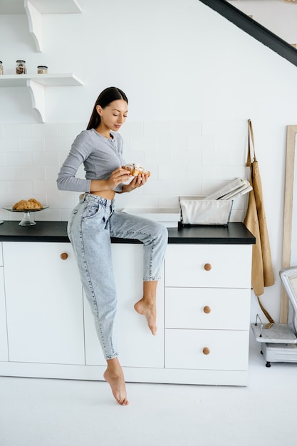 Portrait of rejoicing woman eats tasty croissant at home.