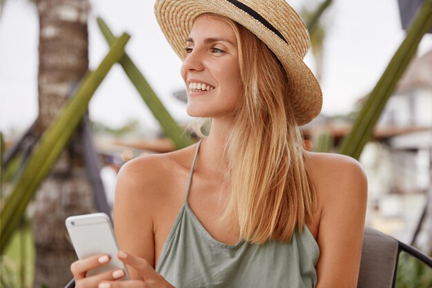 Portrait of relaxed female tourist rests in cafe interior with mobile phone