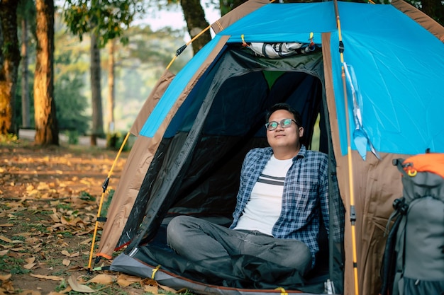 Portrait of Relaxing Asian traveler man glasses looking view while sitting in tent camping Outdoor traveling camping and lifestyle concept