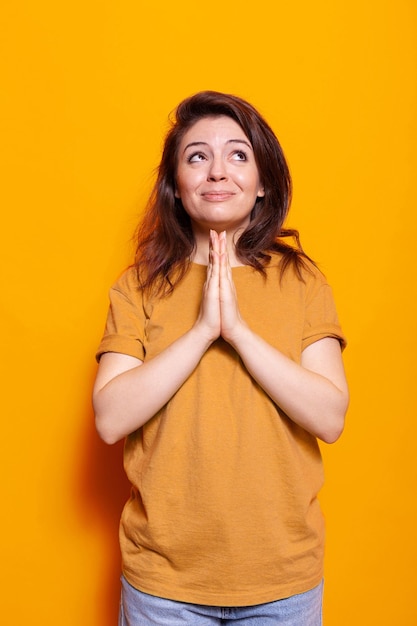 Portrait of religious woman doing gesture with hands to pray to god for miracle. Hopeful person with belief doing prayer for good luck and desire. Positive adult believing in spirituality