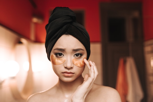 Portrait of sad Asian woman in towel and with gold patches under eyes