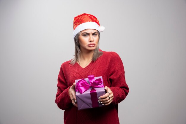 Portrait of sad woman posing with holiday gift on gray background.