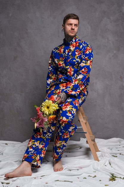 Portrait of a sad young man sitting on stool with flower bouquet in his hand