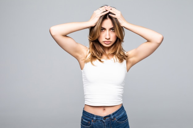 Portrait of sad young woman with hands over head standing over grey wall