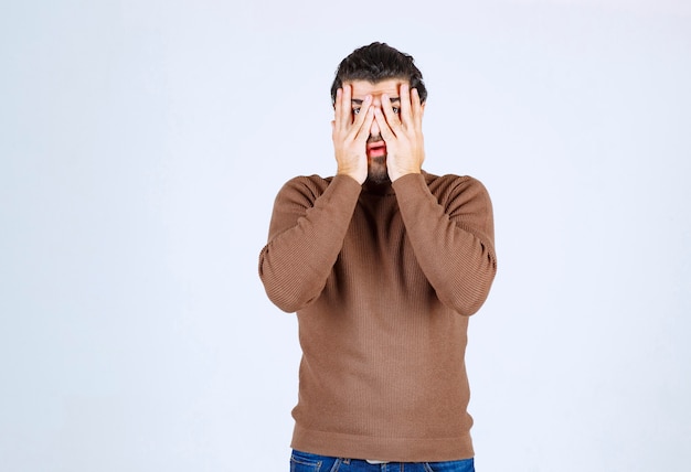 Free photo portrait of a scared man covering his face with palms and looking through fingers isolated