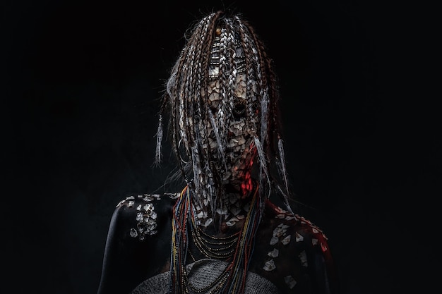 Free photo portrait of a scary african shaman female with a petrified cracked skin and dreadlocks on a dark background. make-up concept.