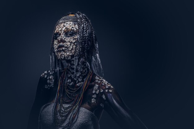 Portrait of a scary African shaman female with a petrified cracked skin and dreadlocks on a dark background. Make-up concept.