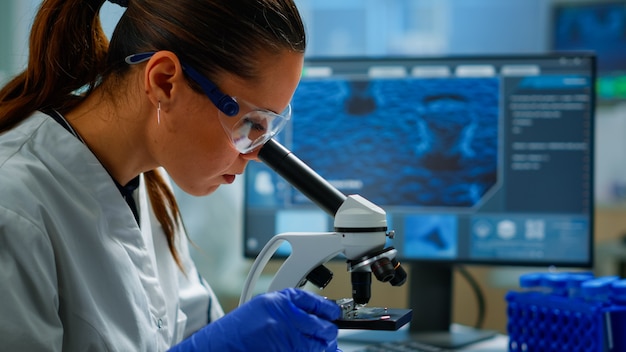 Free photo portrait of scientist looking under microscope in medical development laboratory, analyzing petri dish sample. medicine, biotechnology research in advanced pharma lab, examining virus evolution