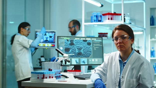 Free Photo portrait of scientist nurse looking tired at camera sitting in modern equipped laboratory late at night. team of specialists examining virus evolution using high tech for research, vaccine development