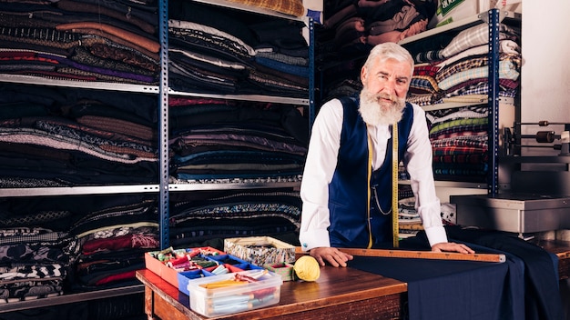 Free photo portrait of a senior male fashion designer in his shop looking at camera