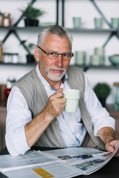 Portrait of senior man with coffee cup in his hand reading newspaper