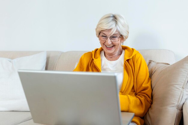 Portrait of senior woman sitting at home on the sofa and working on her laptop Older lady surfing the net or having video call from home and feeling exiciting Holding cup of coffee or tea