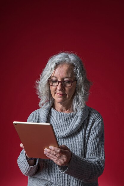 Portrait of a senior woman using digital tablet against red backdrop