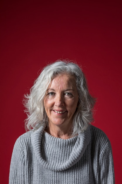 Portrait of a senior woman with short grey hair against red background