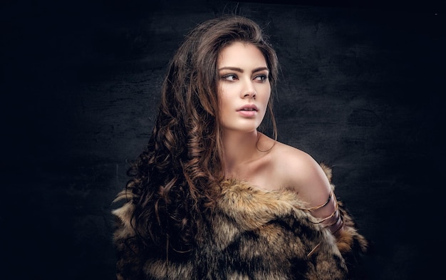 Free photo portrait of a sensual brunette female dressed in a warm fur coat on grey background in a deep shadow.