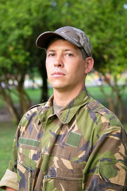 Portrait of serious man in military camouflage uniform standing in park,