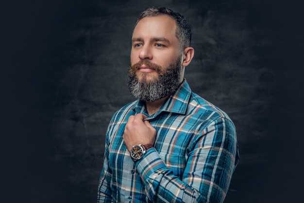 Portrait of serious middle age bearded male dressed in plaid flannel shirt over grey background.