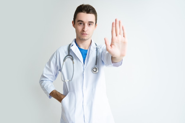 Portrait of serious young male doctor showing stop gesture