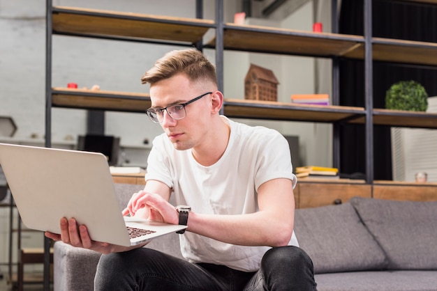 Portrait of a serious young man sitting on sofa using laptop