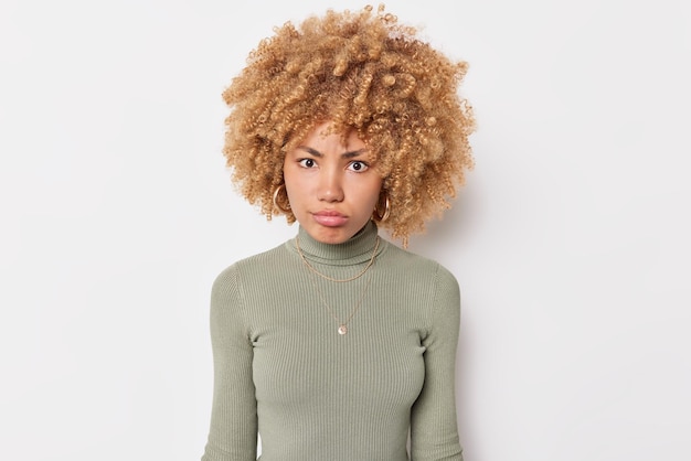 Free photo portrait of serious young woman has strict angry expression focused at camera dressed in casual jumper poses against white background listens someone attentively analyzes received information