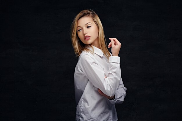 Portrait of sexy blonde female in a white man's shirt isolated on dark grey background.