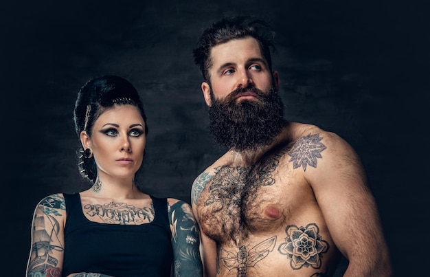 Free photo portrait of shirtless, tattooed bearded hipster male and brunette female with tattoo ink on her torso over dark grey background.