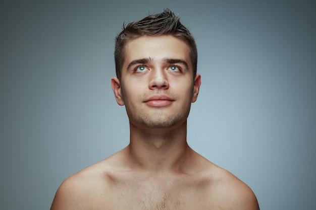 Portrait of shirtless young man isolated on grey studio background. Caucasian healthy male model looking up and posing. Concept of men's health and beauty, self-care, body and skin care.